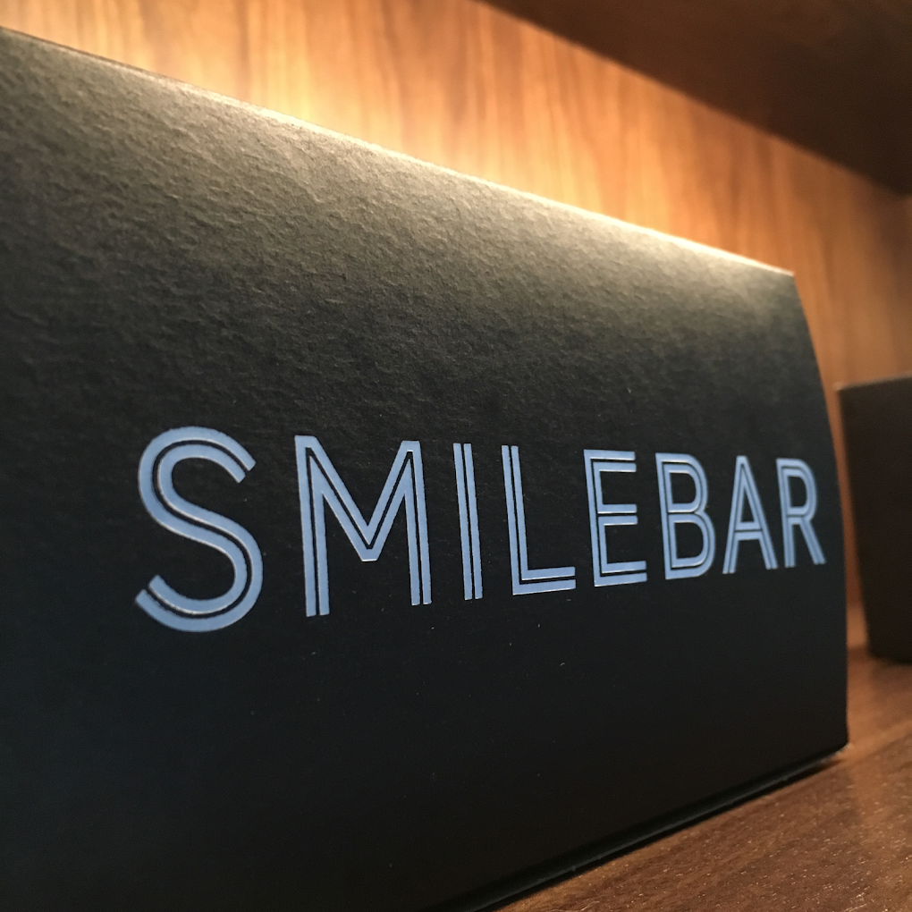 Smilebar letterpress signage in metallic on charcoal cardstock, lit warmly against walnut