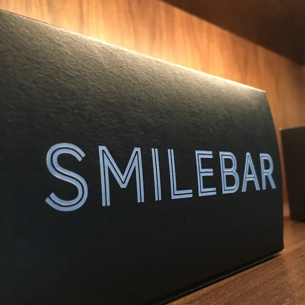 Smilebar letterpress signage in metallic on charcoal cardstock, lit warmly against walnut